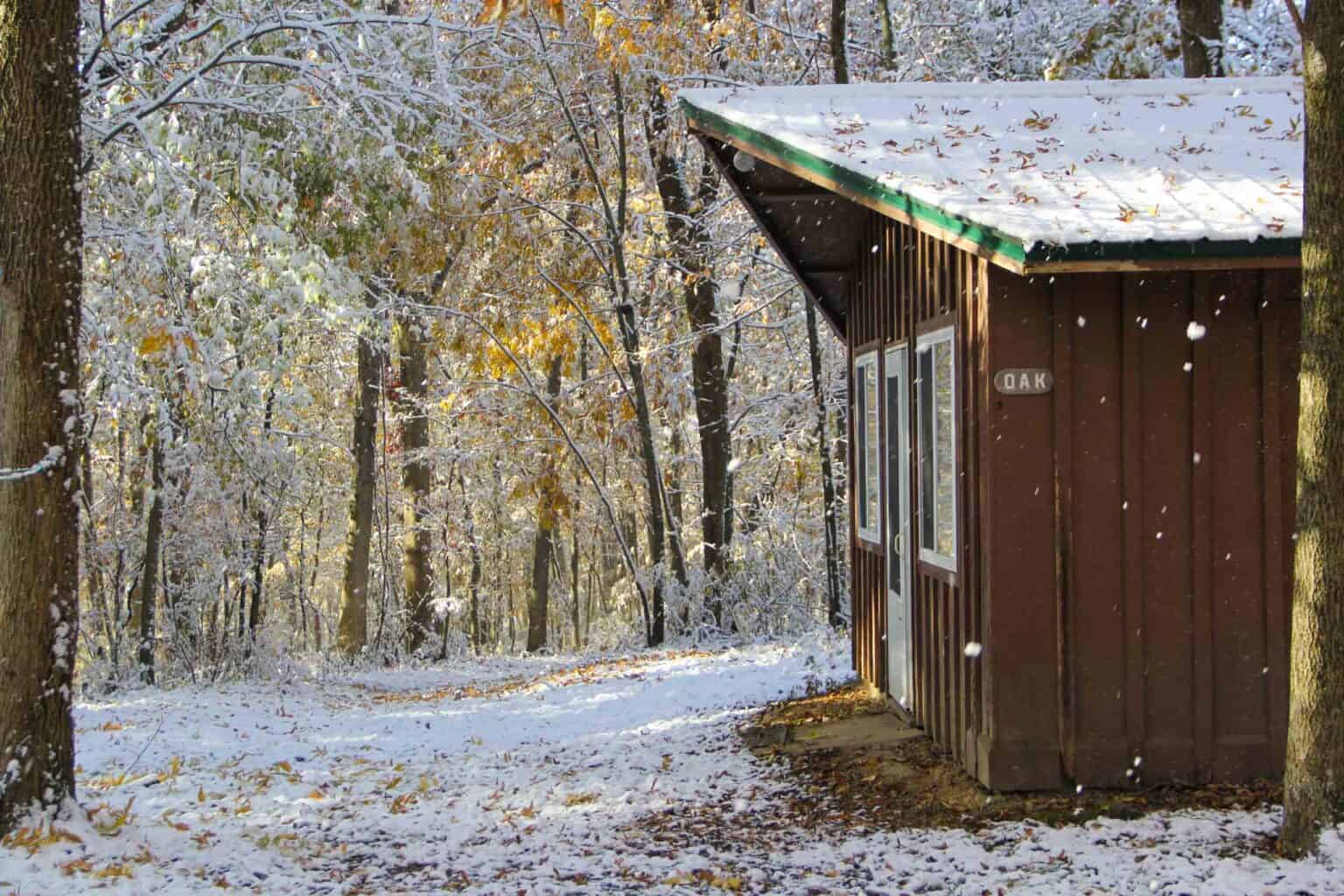A summer camp cabin in the woods of Iowa covered in snow.