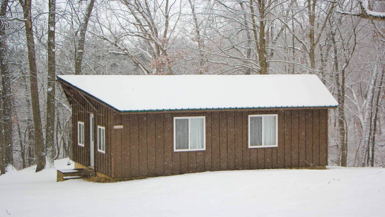A cabin in the Iowa woods covered in snow.
